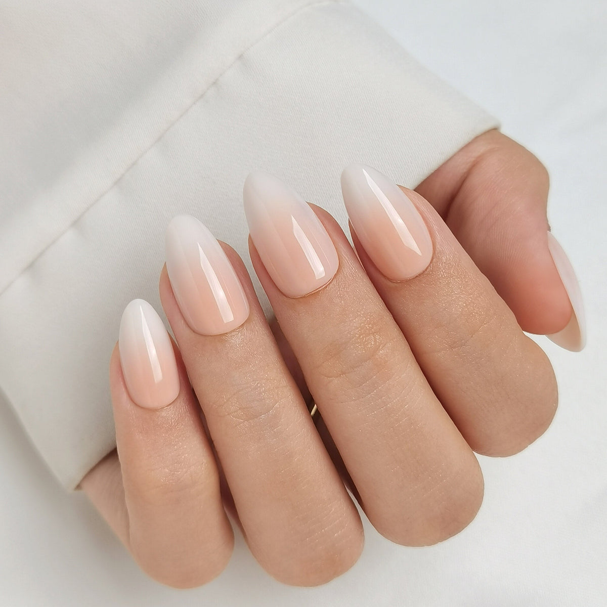 Hand mit Baby Boomer Light Press On Nägeln in Short Almond, heller Nude-Ton am Nagelbett, der weich in ein milchiges Weiß an der Spitze übergeht