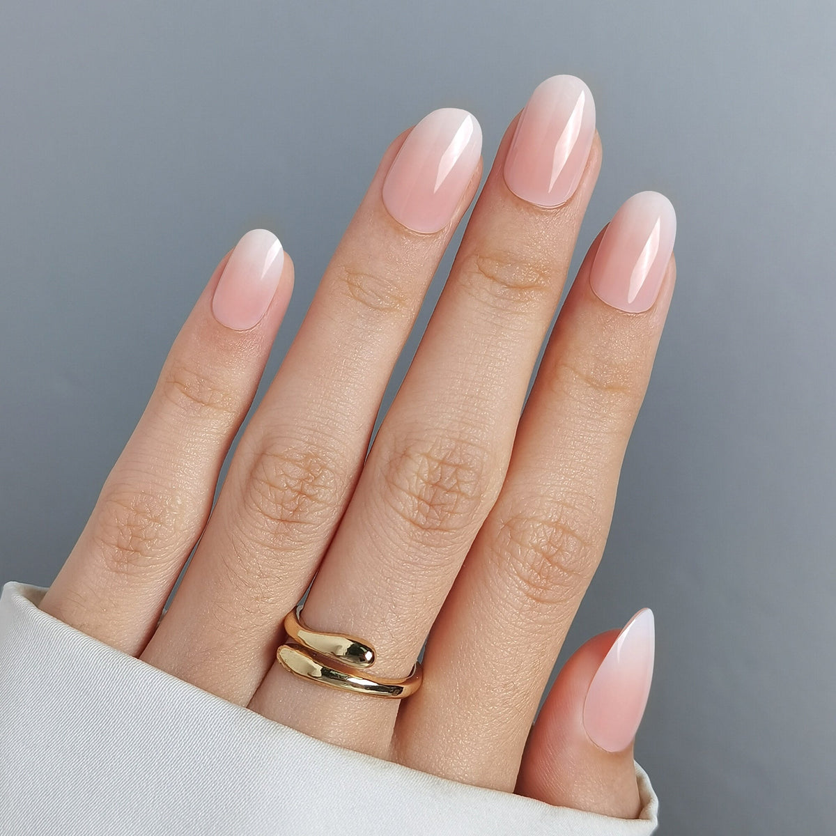 Hand mit Baby Boomer Press On Nägeln in Medium Round, nudefarbenes Nagelbett mit fließendem Übergang in eine weiße Spitze