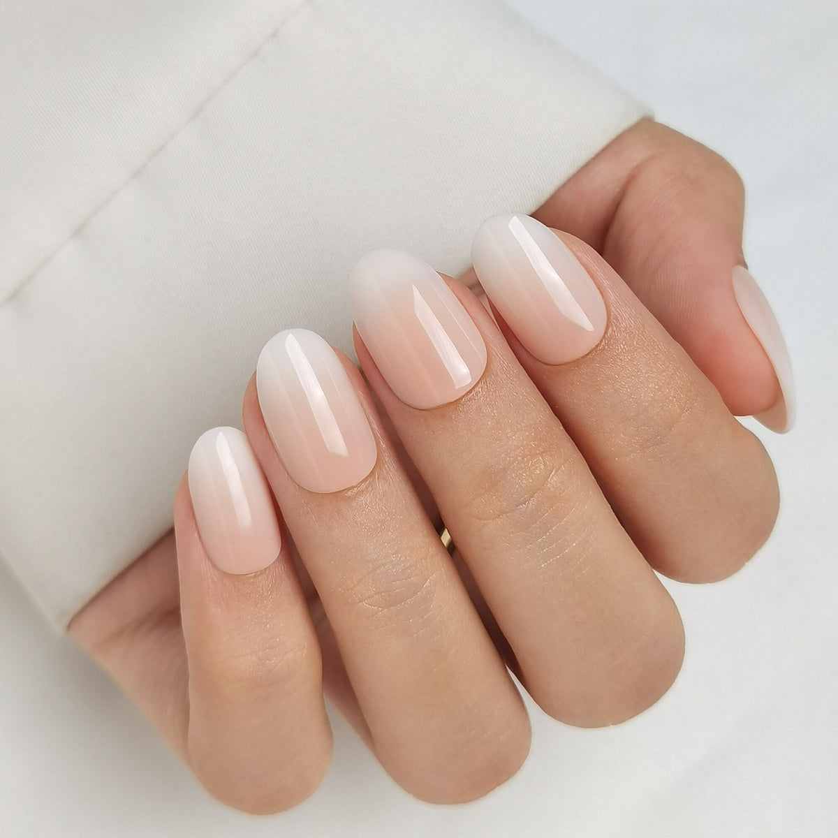 Hand mit Baby Boomer Light Press On Nägeln in Medium Round, heller Nude-Ton am Nagelbett, der weich in ein milchiges Weiß an der Spitze übergeht