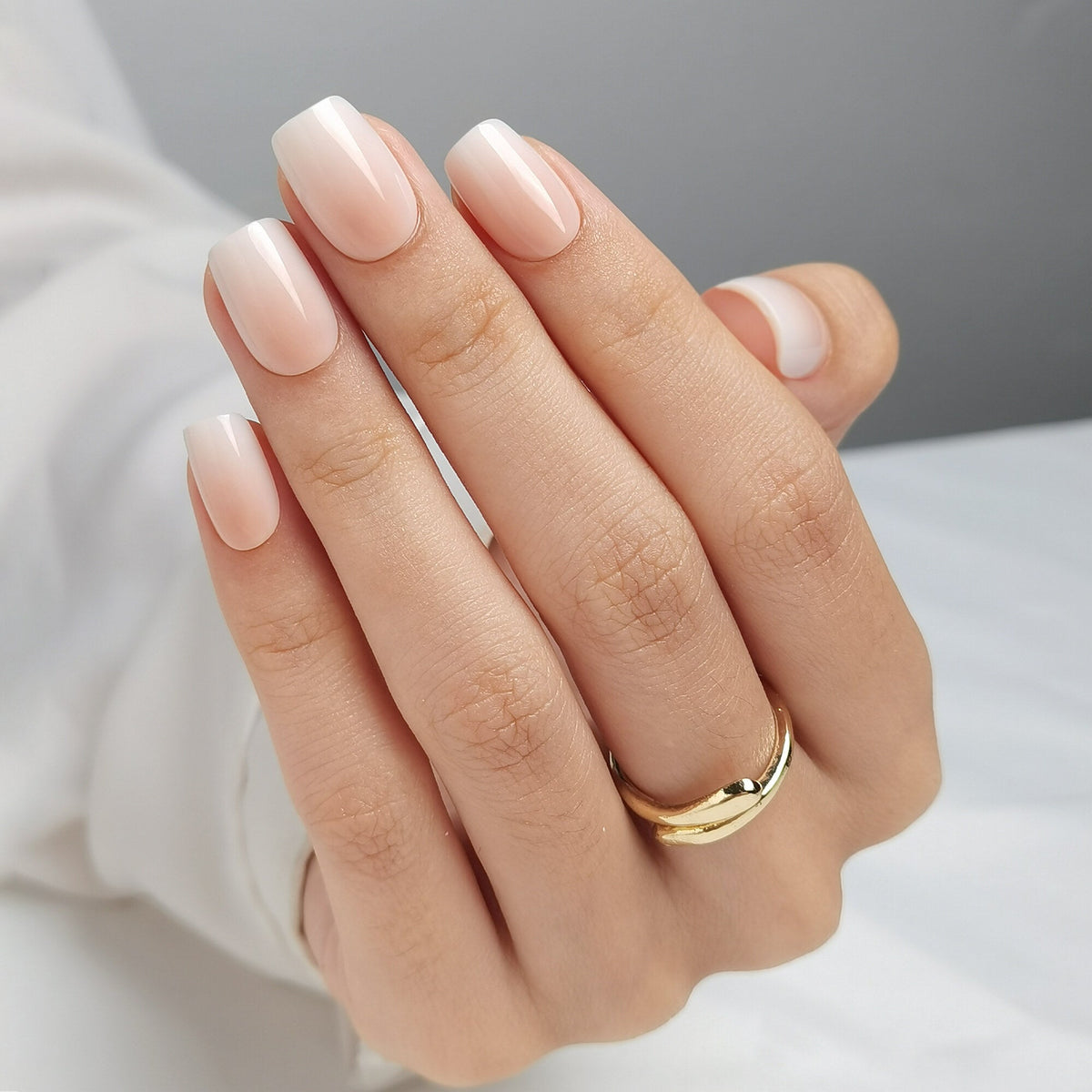 Hand mit Baby Boomer Light Press On Nägeln in Short Square, heller Nude-Ton am Nagelbett, der weich in ein milchiges Weiß an der Spitze übergeht