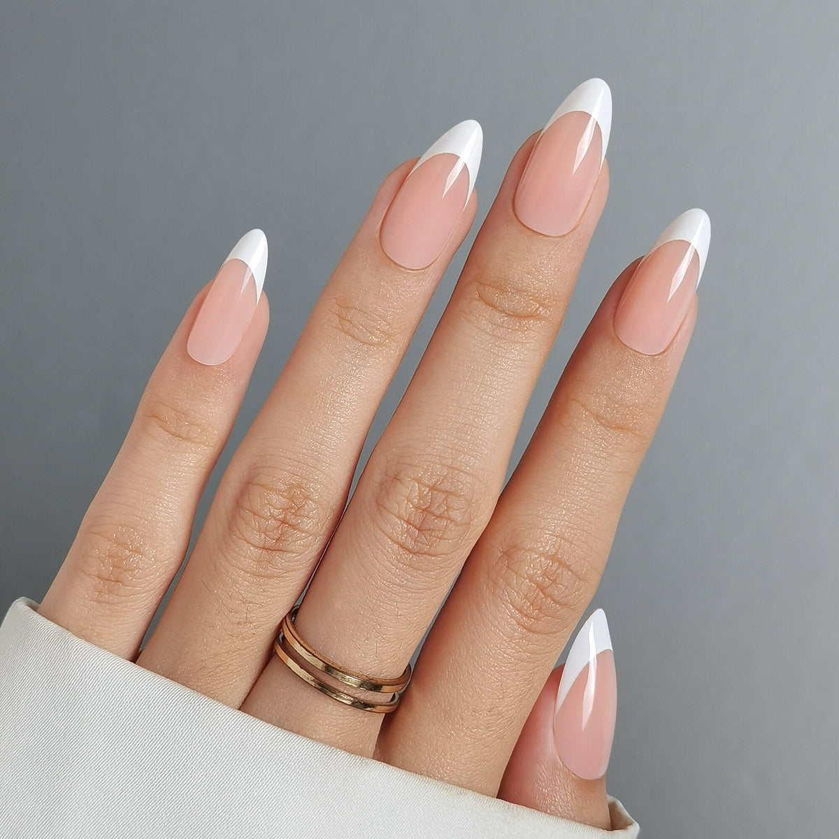 Hand mit French Nail Nude Press On Nägeln in Medium Almond, warmes Nude am Nagelbett mit einer schmal gezogenen weißen Spitze
