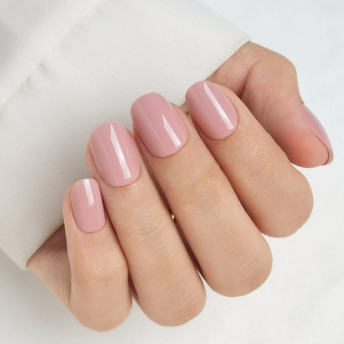 Hand mit Rosy Fusion Press On Nägeln in Short Round, weiches, altrosa getöntes Nude mit hoher Deckkraft und glänzendem Finish